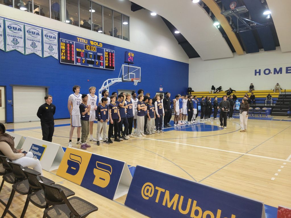 TMU players stand for the Canadian anthem with East York pupils (Trae Dieye)